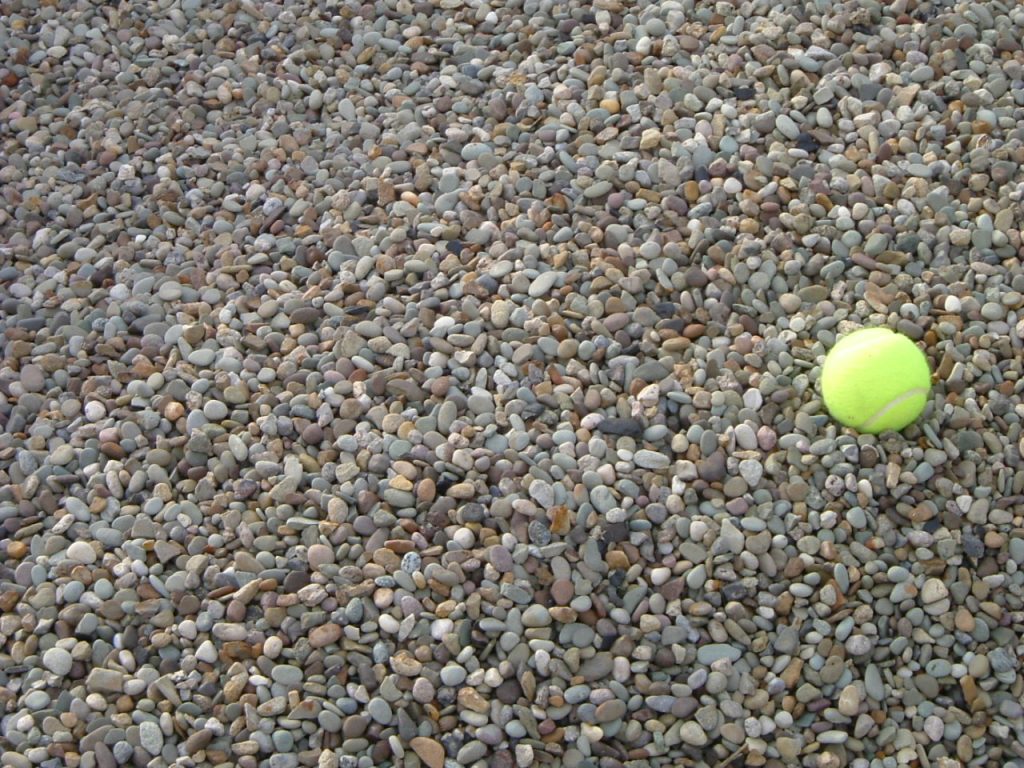 Tan to light gray pea gravel with a yellow tennis ball for scale